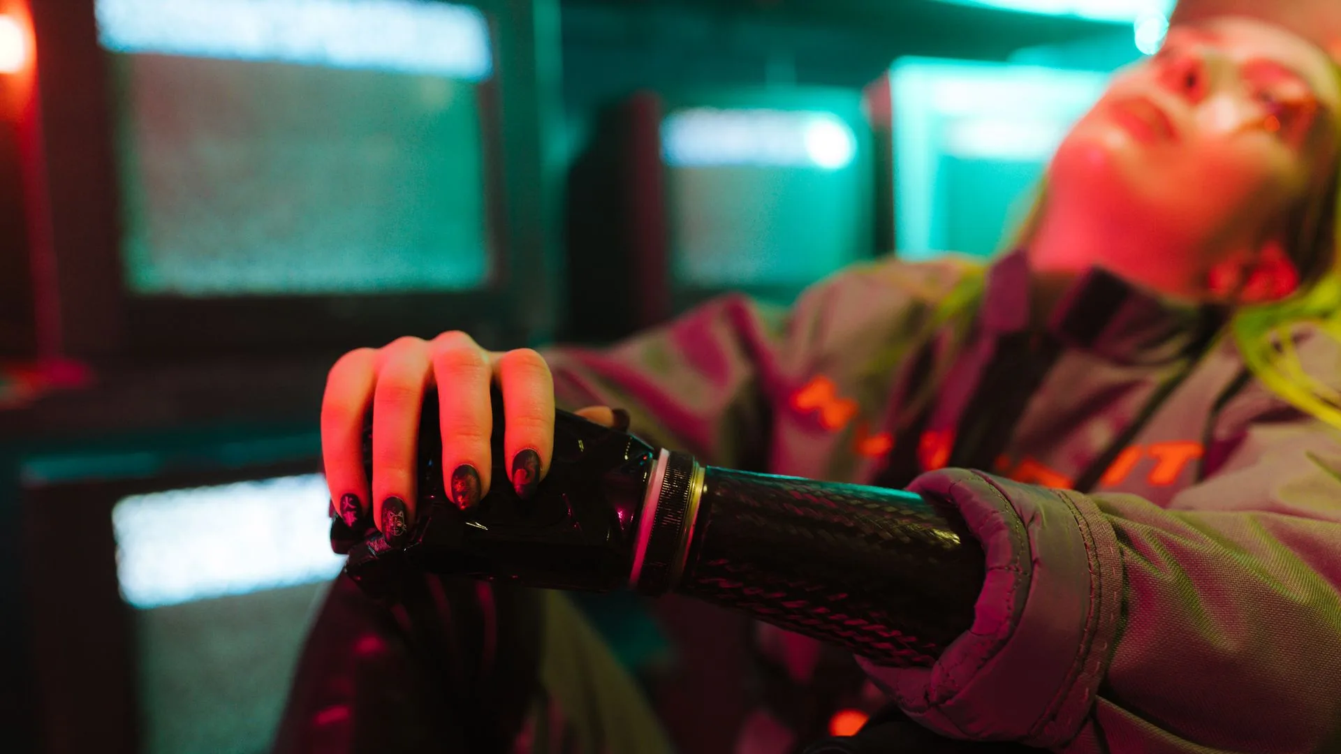 Woman resting a black cybernetic prosthetic arm under teal and magenta neon
