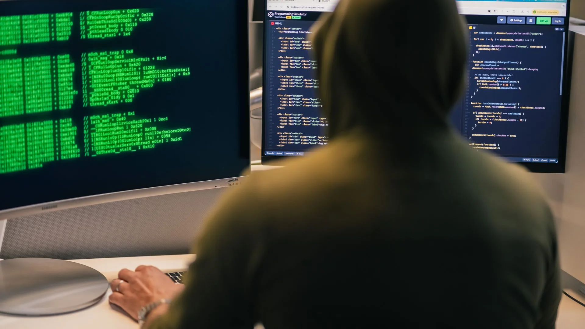 Hooded figure coding between three monitors of green terminal text