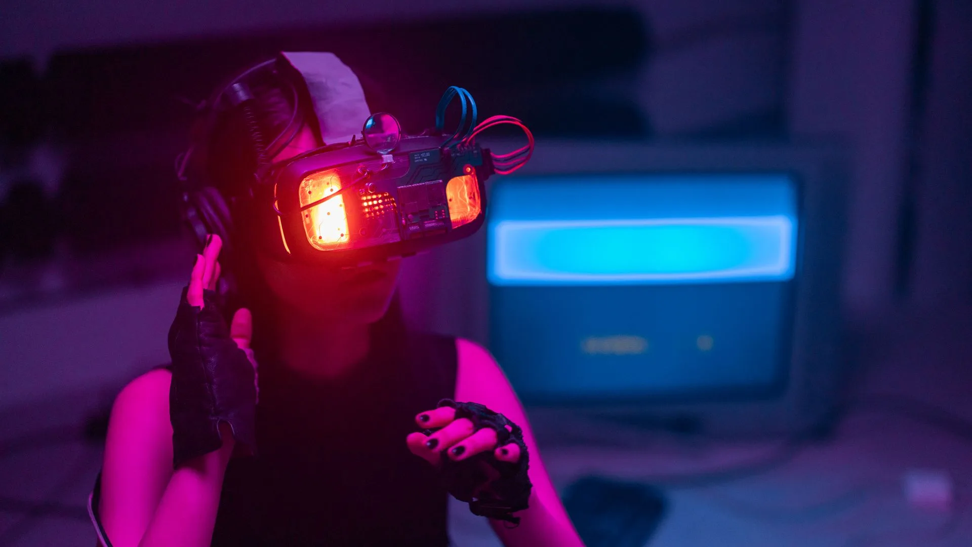 Person wearing a wired cyber-visor headset before a CRT in magenta light